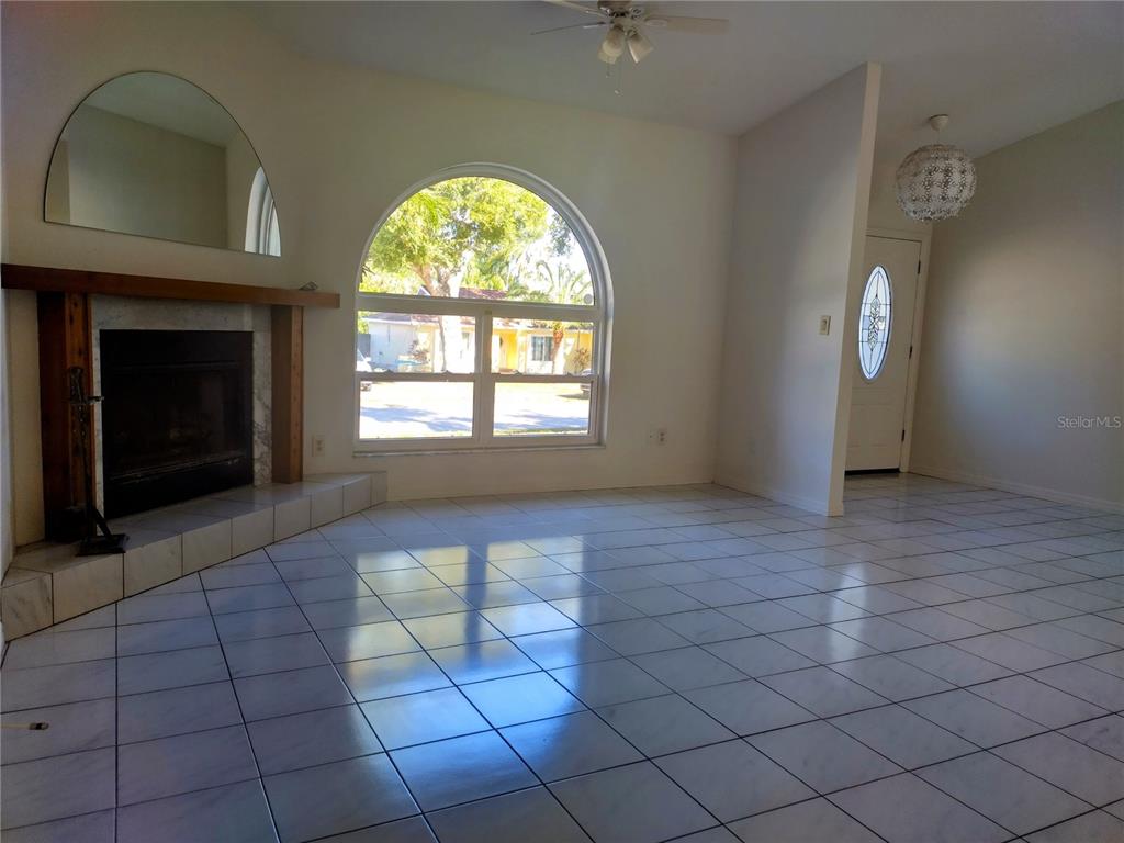 A living room features white tile flooring, a fireplace, and a large arched window — 1936 SPANISH OAKS DRIVE S, PALM HARBOR, FL