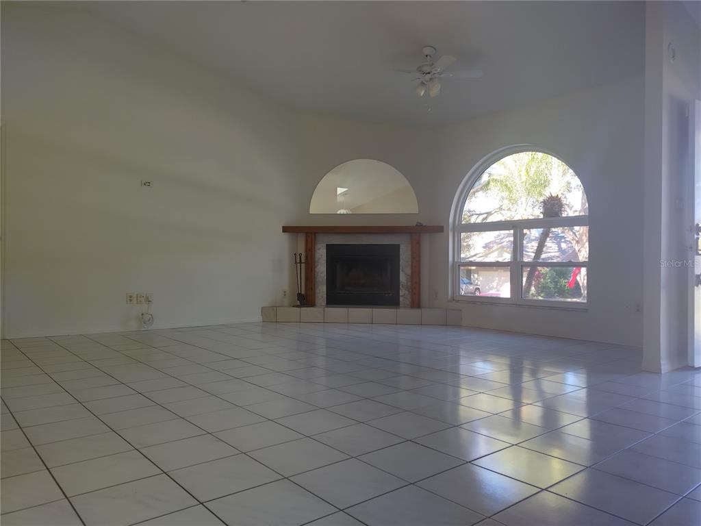 A living room features white tile floors, a fireplace with a mantel, and an arched window — 1936 SPANISH OAKS DRIVE S, PALM HARBOR, FL