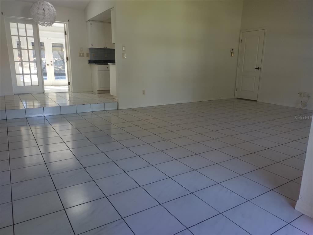 An interior view shows a tiled living area with a kitchen and glass doors beyond — 1936 SPANISH OAKS DRIVE S, PALM HARBOR, FL