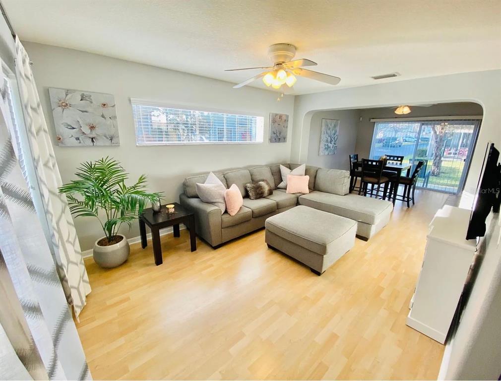 A living room with light wood floors, a gray sectional sofa, and an adjacent dining area — 8013 BOONE DRIVE, LARGO, FL