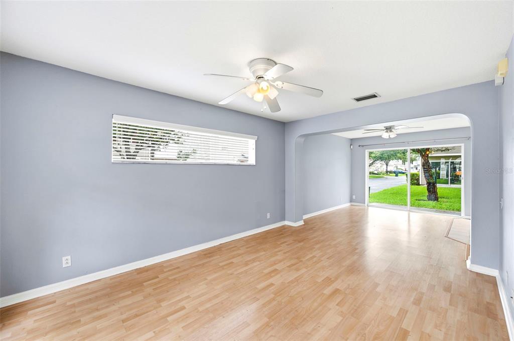 An empty living room with light blue walls, wood-look flooring, and a sliding glass door — 8013 BOONE DRIVE, LARGO, FL