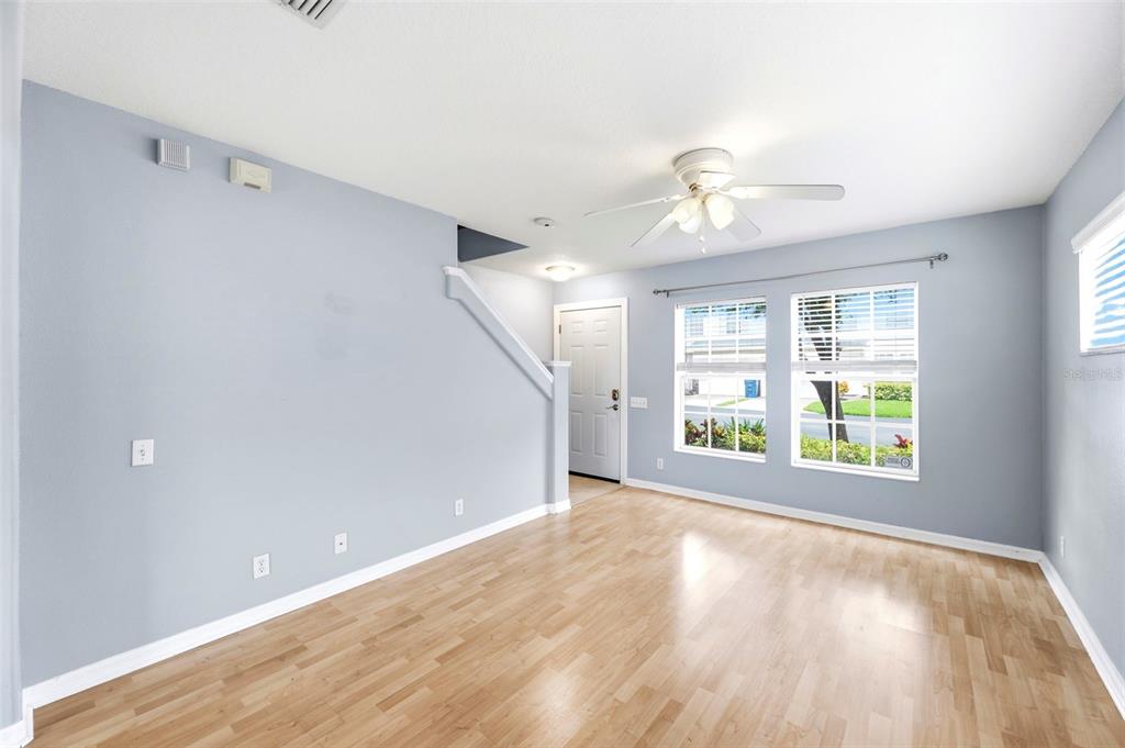 An empty living room features light blue walls, wood-look flooring, and a ceiling fan — 8013 BOONE DRIVE, LARGO, FL
