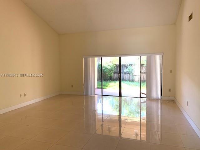 An empty living room with vaulted ceilings, light-colored tile floors, and sliding glass patio doors — 4526 SW 143rd Ct W # 0, Miami FL 33175, MIAMI, FL