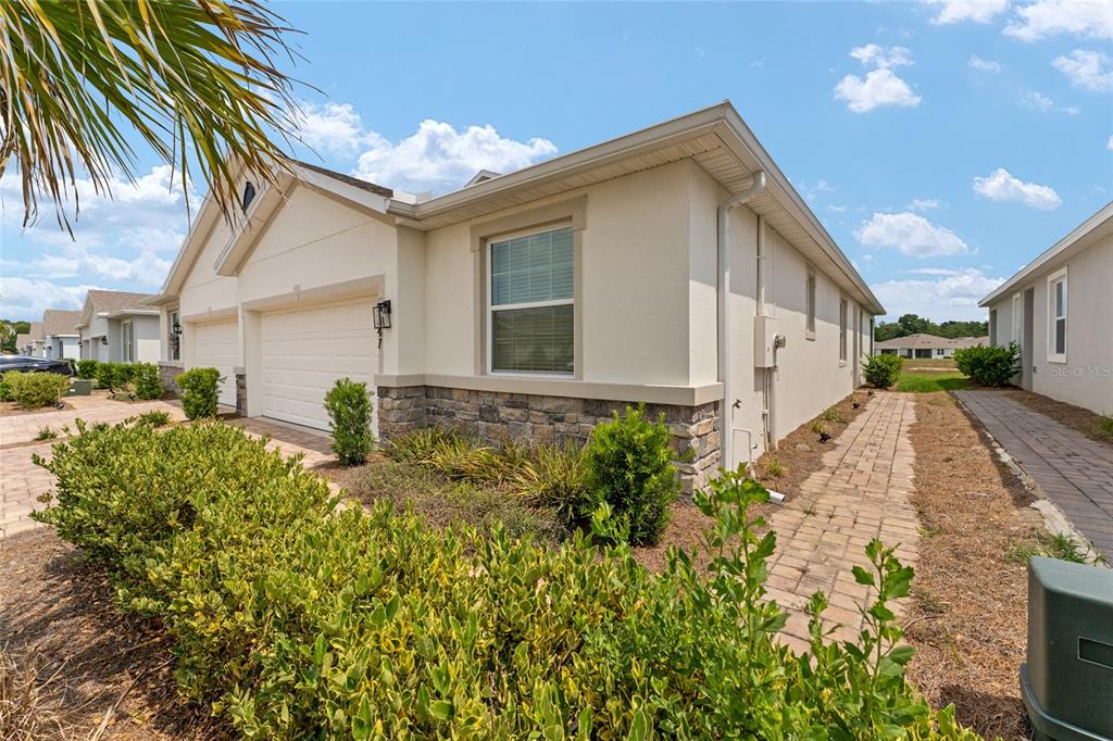 A side view of a beige suburban house with a stone base and brick walkway — 5347 NW 46TH LANE ROAD, OCALA, FL