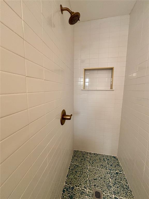 A shower stall with white subway tile walls, a gold-toned fixture, and a mosaic floor — 4415 NW 33RD COURT, GAINESVILLE, FL