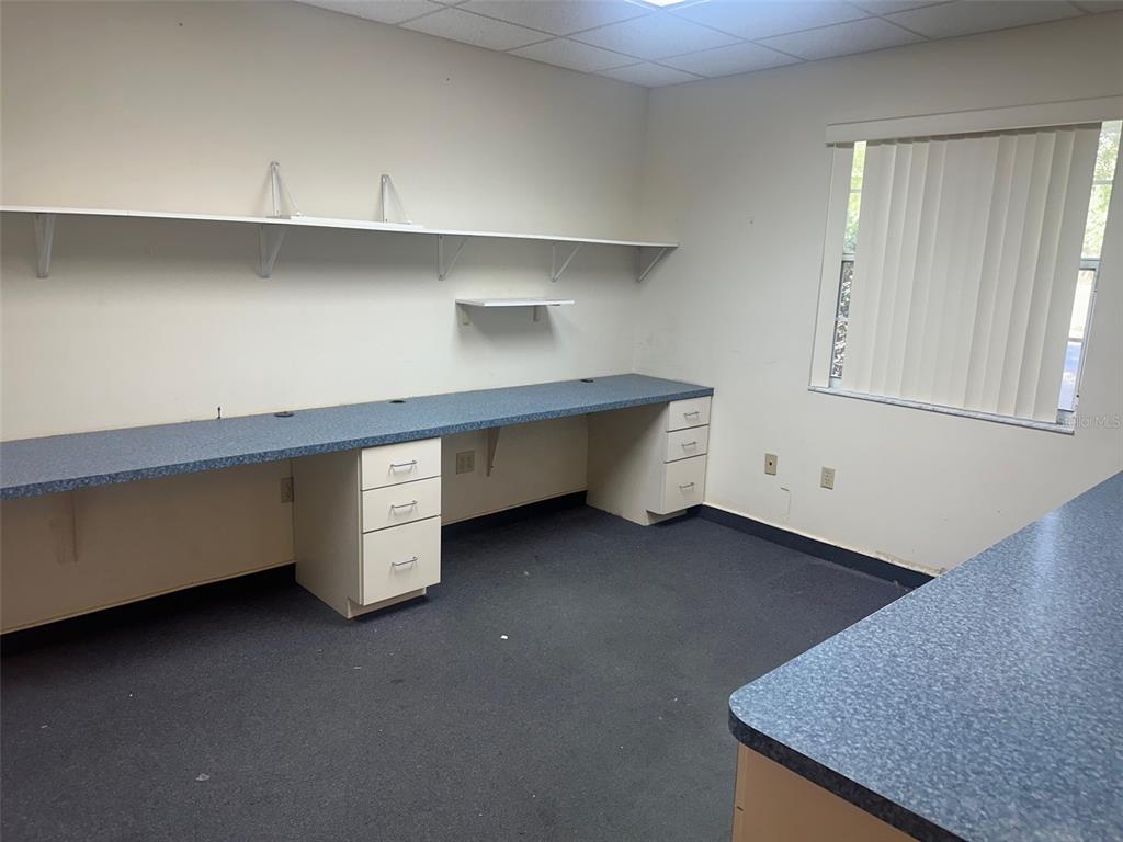 An office space features blue laminate countertops, white drawer cabinets, wall shelving, and a window — 4611 NW 53RD AVENUE UNIT B, GAINESVILLE, FL