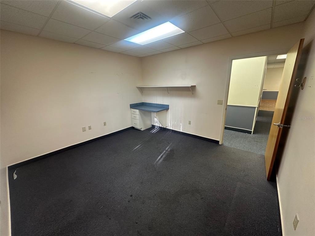 An empty office with dark carpet, a built-in desk, and a shelf on the wall — 4611 NW 53RD AVENUE UNIT B, GAINESVILLE, FL