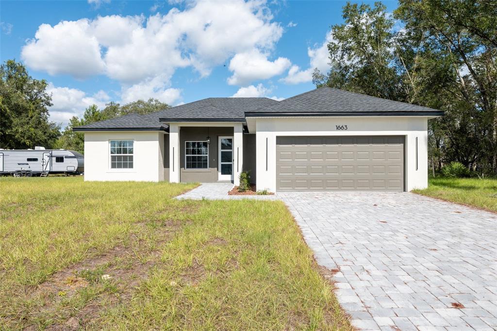 A single-story house with a white stucco exterior, dark roof, and a paved driveway — 1663 SW 167TH STREET, OCALA, FL