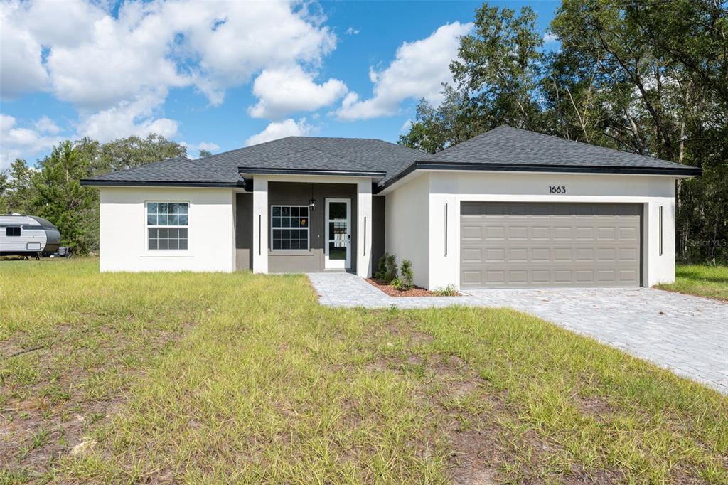 A single-story house with a white exterior, a gray garage door, and a paved walkway — 1663 SW 167TH STREET, OCALA, FL