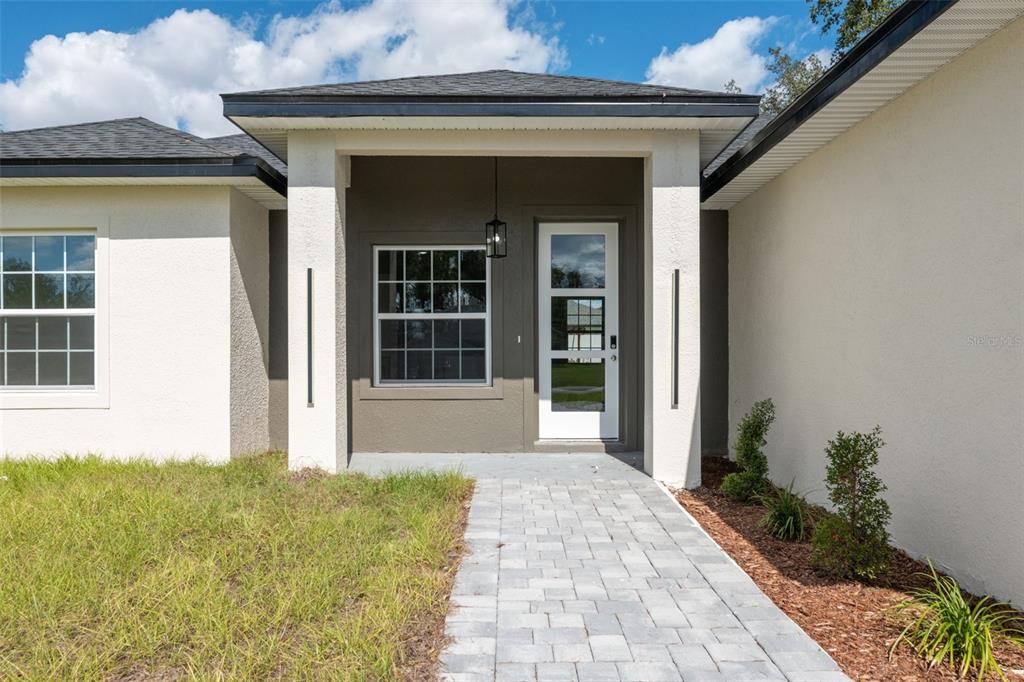 The exterior of a house features a covered entryway with a paved walkway and landscaping — 1663 SW 167TH STREET, OCALA, FL