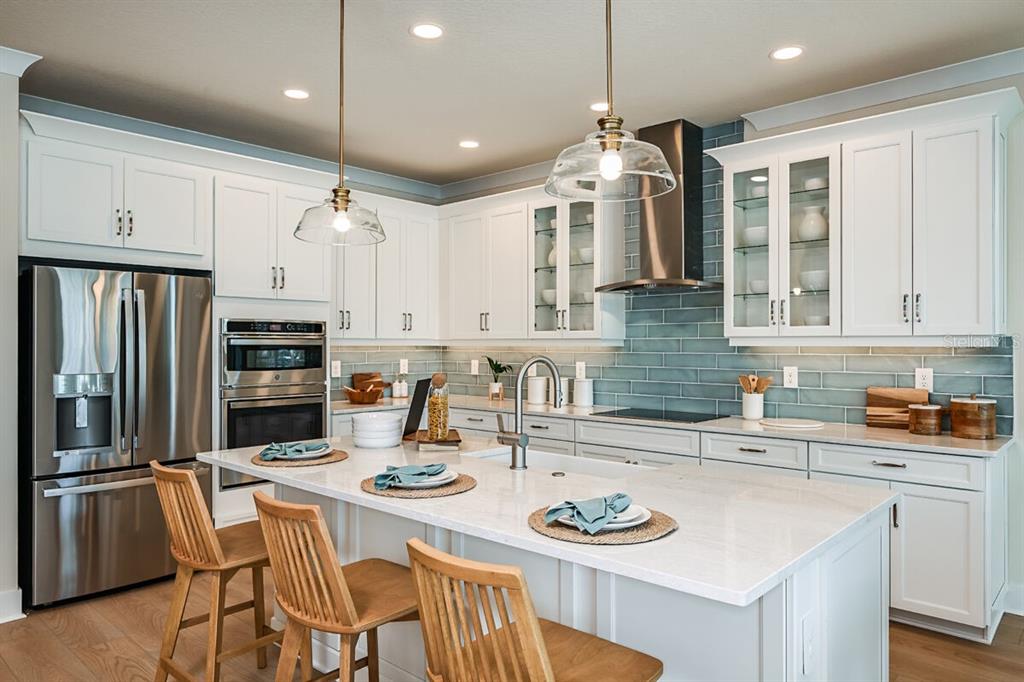 A modern kitchen features white cabinetry, a large island with bar seating, and blue-green backsplash tile — 13685 LOREDO WAY, PUNTA GORDA, FL