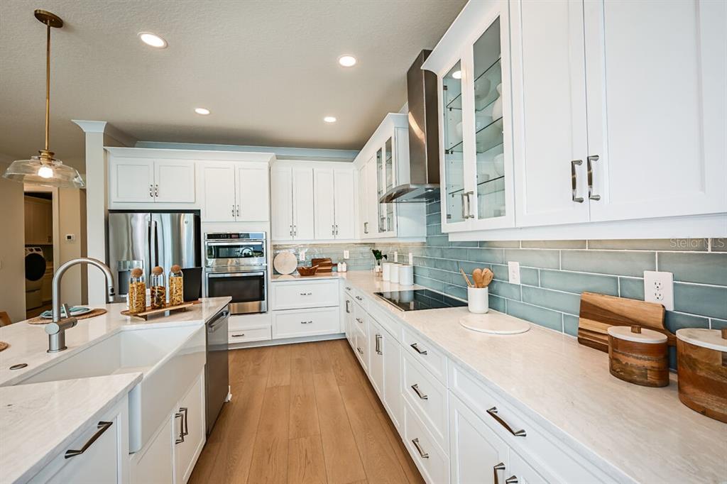 A modern kitchen features white cabinetry, light countertops, a blue subway tile backsplash, and wood flooring — 13685 LOREDO WAY, PUNTA GORDA, FL