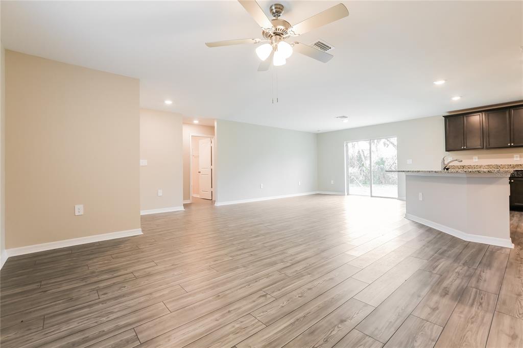 An open-concept living area features wood-look tile flooring, a ceiling fan, and a kitchen peninsula — 2443 ZODIAC STREET, NORTH PORT, FL