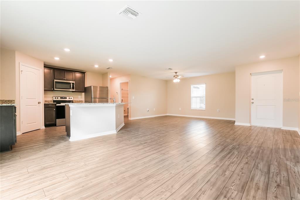 An open-concept kitchen and living area with wood-look flooring, stainless steel appliances, and white cabinets — 2443 ZODIAC STREET, NORTH PORT, FL