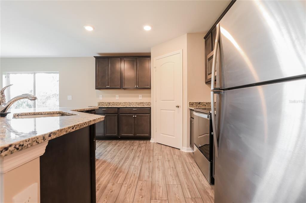 A kitchen features dark wood cabinets, granite countertops, stainless steel appliances, and wood-look flooring — 2443 ZODIAC STREET, NORTH PORT, FL