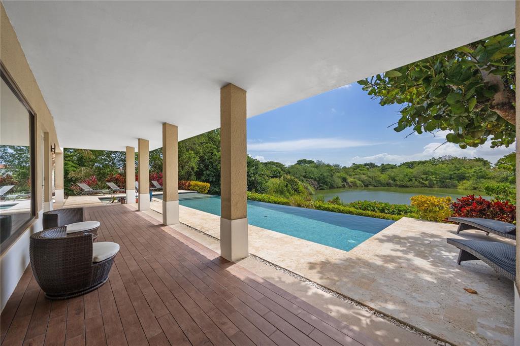 A covered patio with wood flooring overlooks an infinity pool and a natural lake — 403 CAMINO DE LOS JOBANES, DORADO, PR