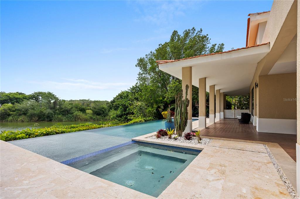 An infinity pool and spa overlook a lake from a covered patio with stone flooring — 403 CAMINO DE LOS JOBANES, DORADO, PR