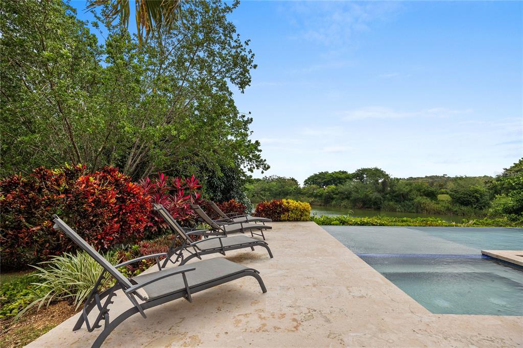 Three lounge chairs sit on a stone pool deck overlooking a lake and lush greenery — 403 CAMINO DE LOS JOBANES, DORADO, PR
