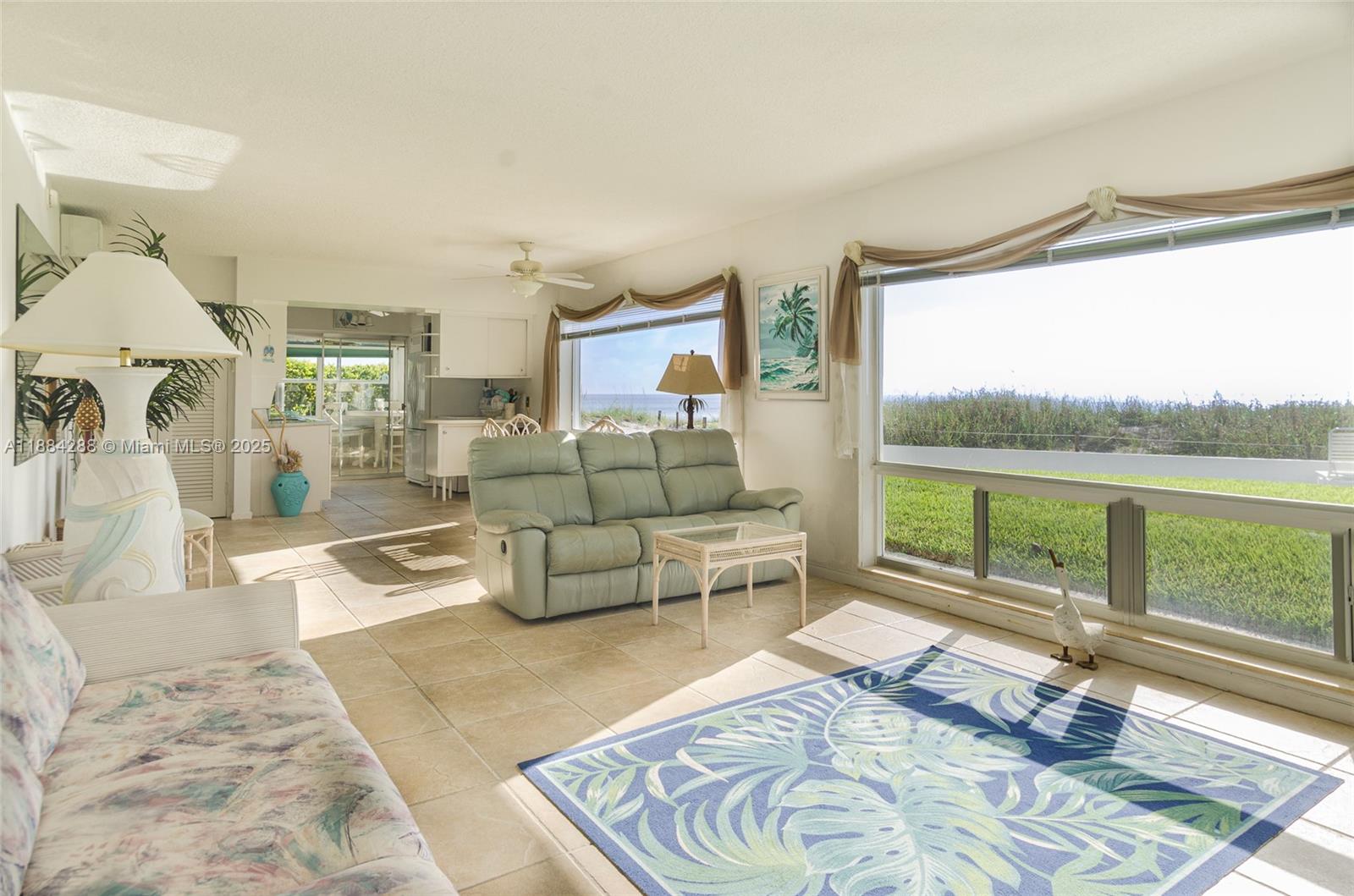 A living room features tile floors, a light green sofa, and large windows overlooking grass — 1470 S Ocean Blvd # 1201, Pompano Beach FL 33062, POMPANO BEACH, FL