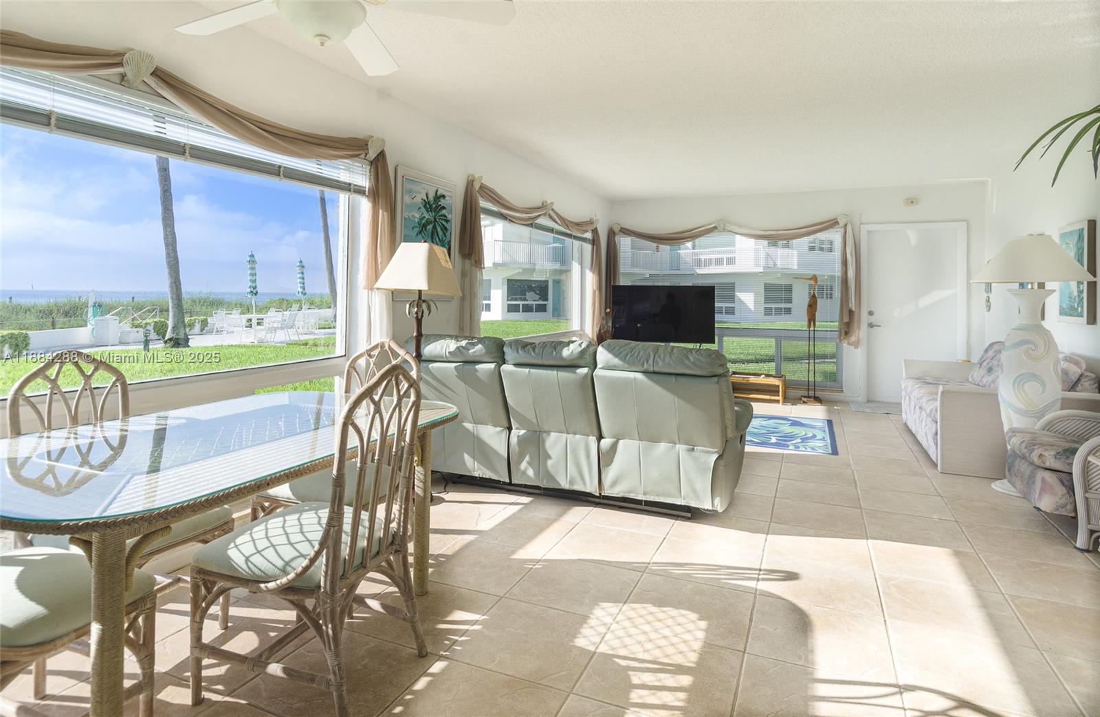 A bright living and dining area features tile floors, rattan furniture, and large ocean-view windows — 1470 S Ocean Blvd # 1201, Pompano Beach FL 33062, POMPANO BEACH, FL