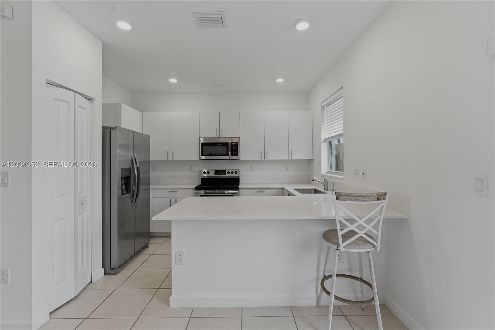 A modern kitchen features white cabinets, stainless steel appliances, and a white quartz breakfast bar — 16314 SW 291 ST # 16314, Miami FL 33033, MIAMI, FL