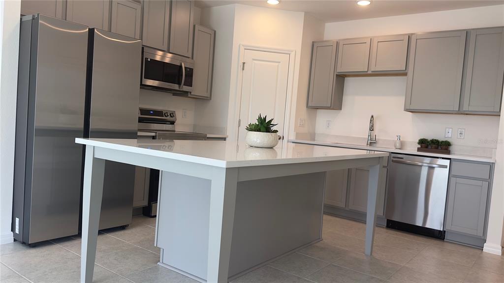 A kitchen features gray cabinets, stainless steel appliances, a white island, and light tile flooring — 3879 ACADEMIA AVENUE, LAKELAND, FL