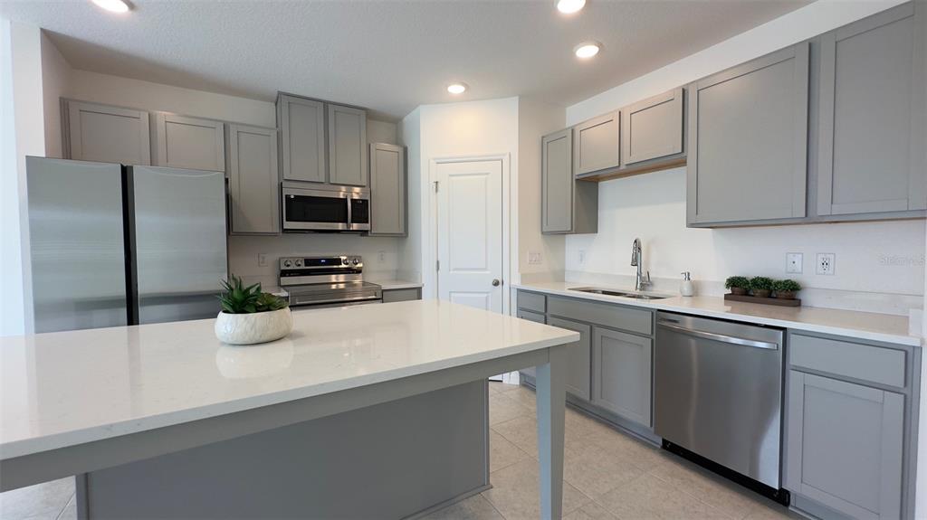 A kitchen features gray cabinets, stainless steel appliances, a white island, and light-colored countertops — 3879 ACADEMIA AVENUE, LAKELAND, FL