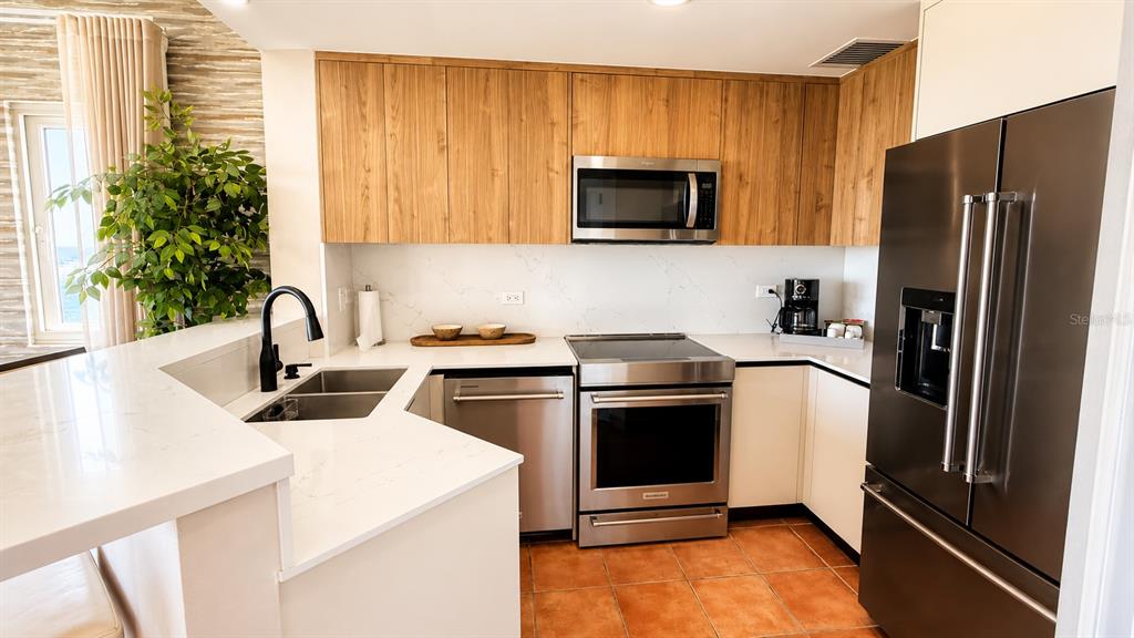 A kitchen features wood-toned cabinetry, stainless steel appliances, white countertops, and terracotta tile flooring — 987 CARR PR UNIT 1, FAJARDO, PR
