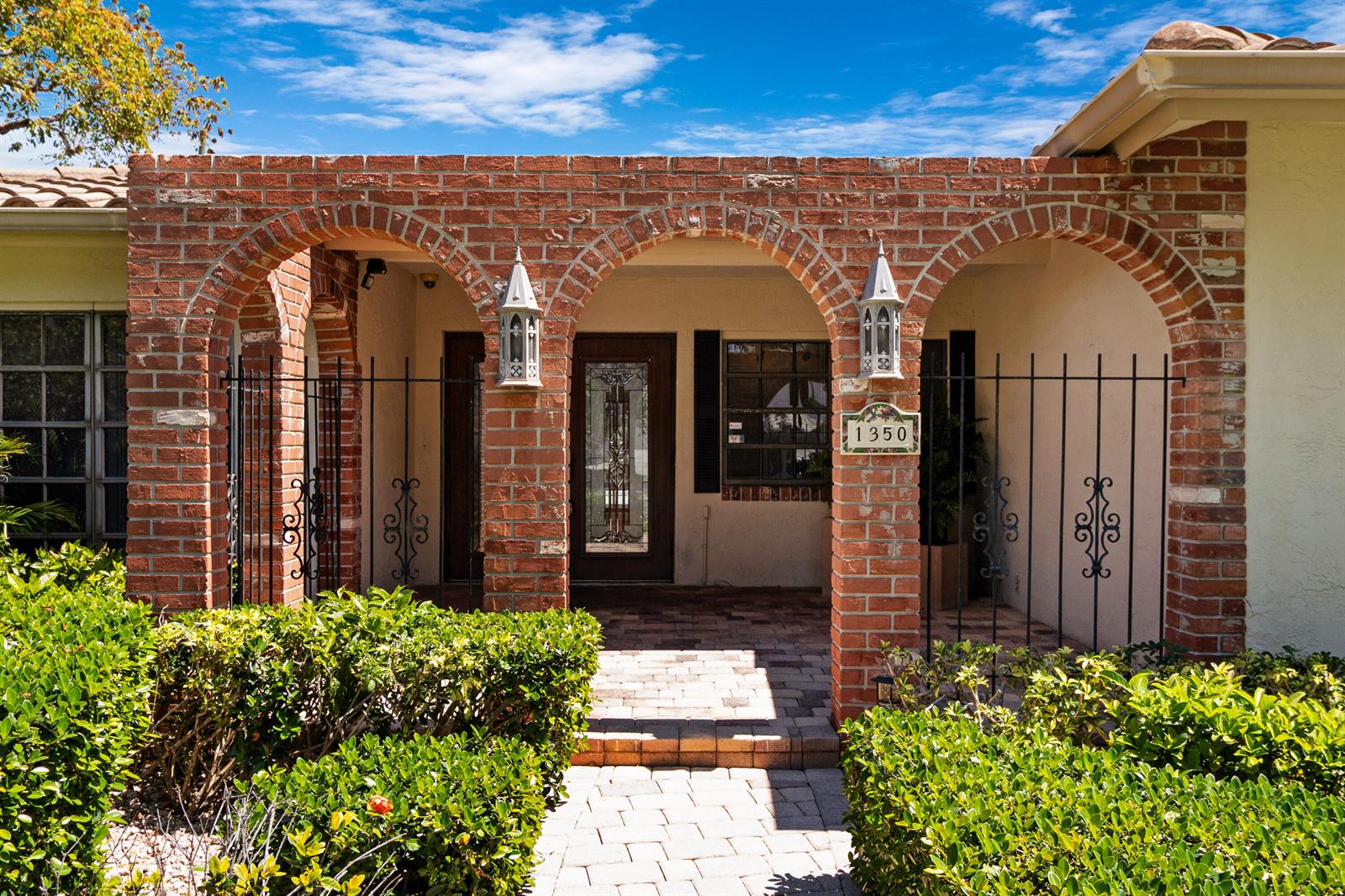 The exterior of a house features a brick arched entryway with iron gates and landscaping — 1350 W Terra Mar Drive, Pompano Beach FL 33062, POMPANO BEACH, FL