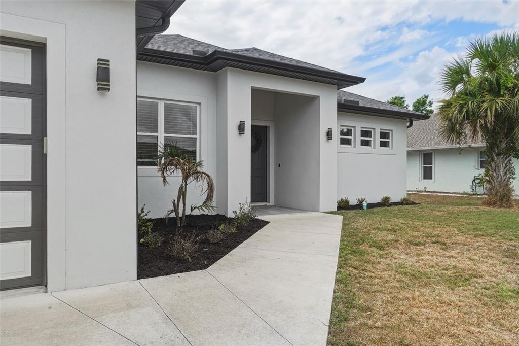 A white stucco house exterior features a concrete walkway leading to a recessed front door — 4143 UNION LANE, NORTH PORT, FL