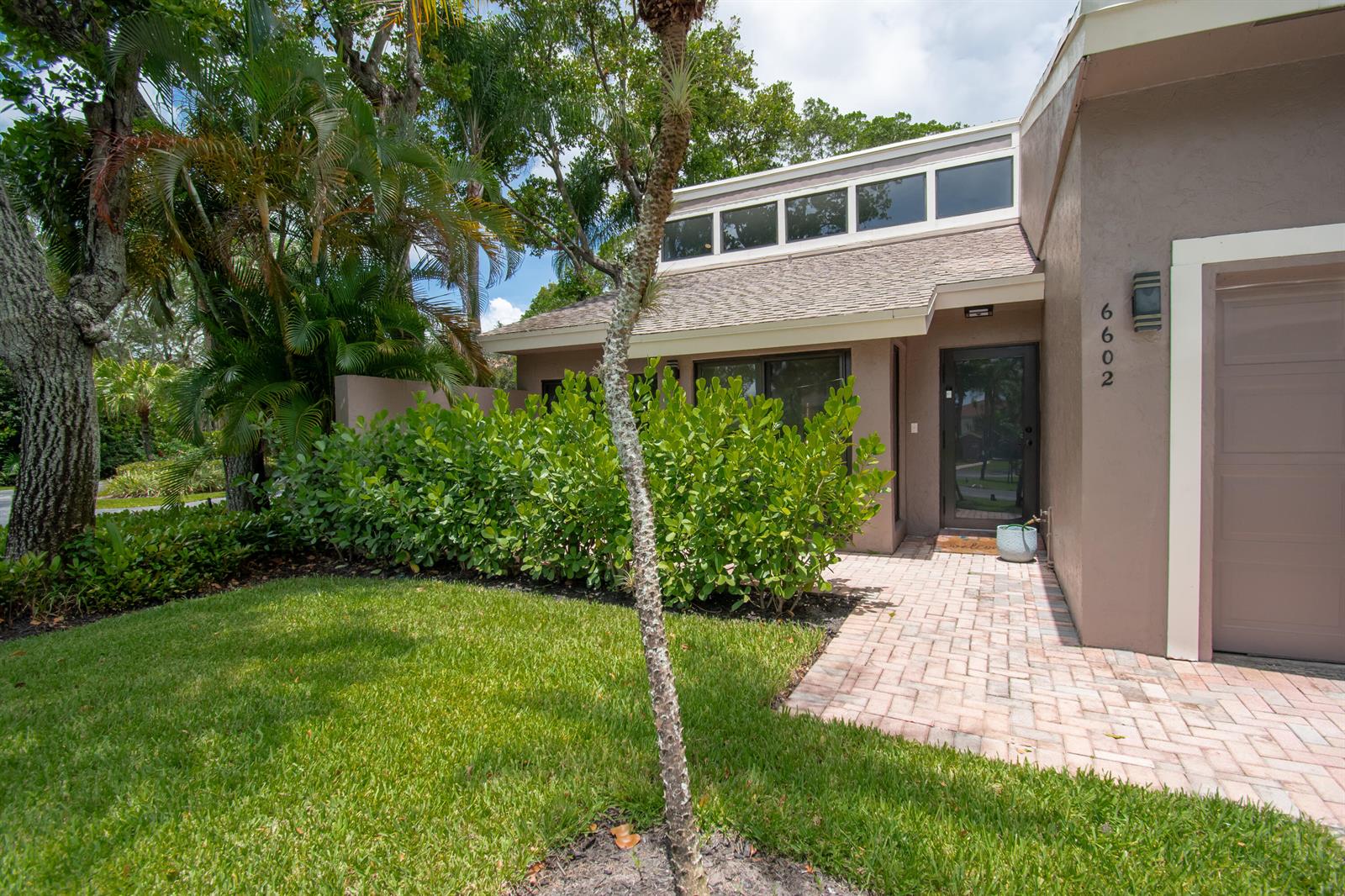 The exterior of a tan house features a brick walkway, green landscaping, and a garage — 6602 Thornhill Court, Boca Raton FL 33433, BOCA RATON, FL