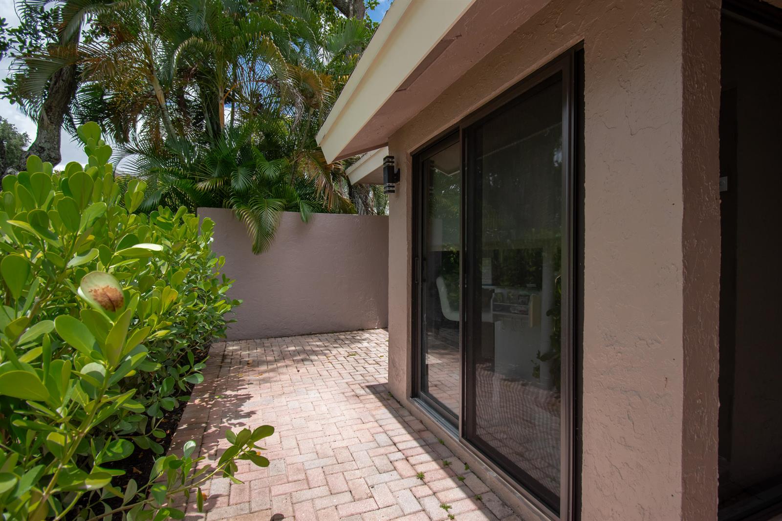 A paved patio area sits beside a house with sliding glass doors and lush landscaping — 6602 Thornhill Court, Boca Raton FL 33433, BOCA RATON, FL