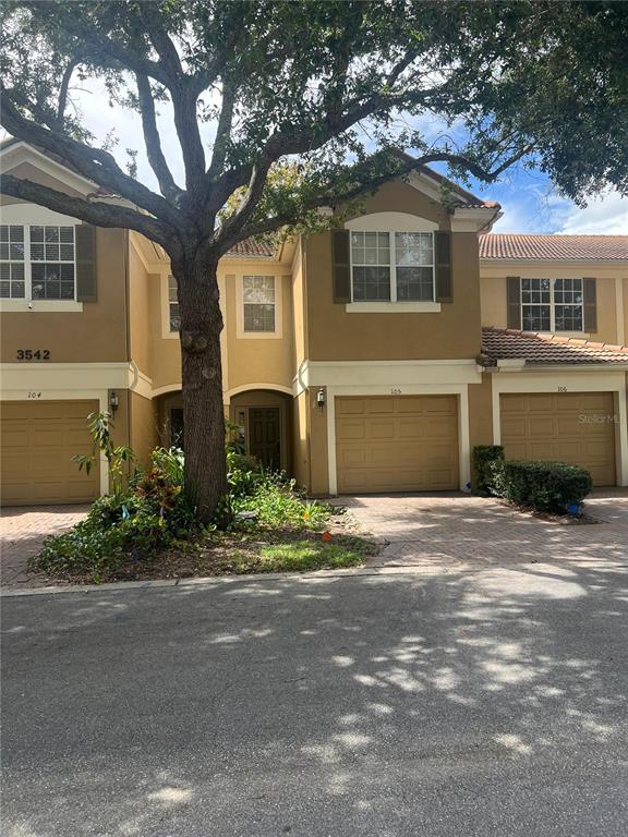 A row of tan townhouses with beige garage doors and a large tree in front — 3542 SHALLOT DRIVE, ORLANDO, FL