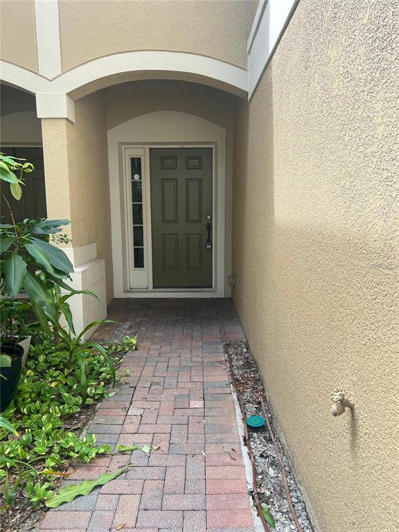 A paved walkway leads to a green front door with a side window under an archway — 3542 SHALLOT DRIVE, ORLANDO, FL