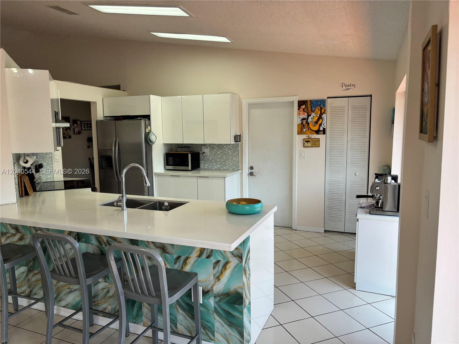 A kitchen features a white island with a teal marble-patterned base and gray bar stools — 18713 NW 78th Ct, Hialeah FL 33015, HIALEAH, FL