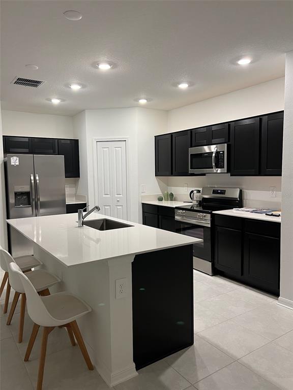 A kitchen features black cabinets, white countertops, a center island, and stainless steel appliances — 1334 DIEGO TERRACE, WINTER HAVEN, FL
