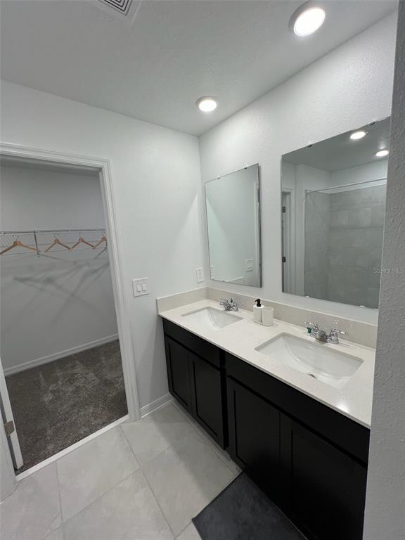 A bathroom features a double vanity with dark cabinets, quartz countertops, and an adjacent walk-in closet — 1334 DIEGO TERRACE, WINTER HAVEN, FL