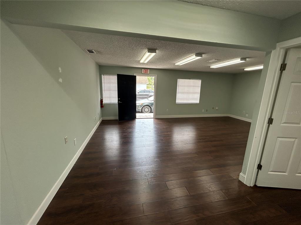 An empty room features dark wood-look flooring, light green walls, and an open exit door — 2945 NE 3RD STREET UNIT 201, OCALA, FL