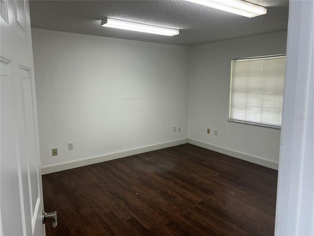 An empty room with white walls, dark wood-look flooring, and two ceiling-mounted fluorescent light fixtures — 2945 NE 3RD STREET UNIT 201, OCALA, FL