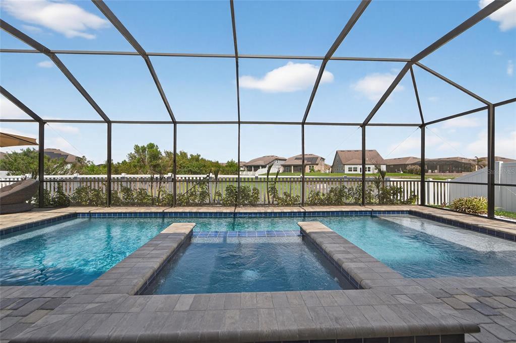 A screened-in swimming pool and spa with stone coping and a white fence background — 13816 GALWAY SAND ROAD, RIVERVIEW, FL