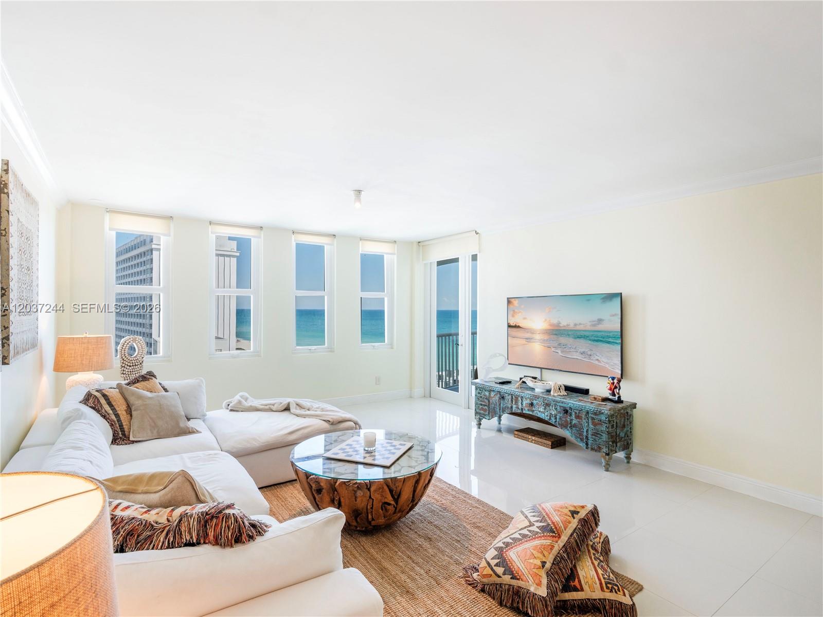A bright living room features a white sectional sofa, a wooden coffee table, and ocean views — 5401 Collins Ave # 1013, Miami Beach FL 33140, MIAMI BEACH, FL