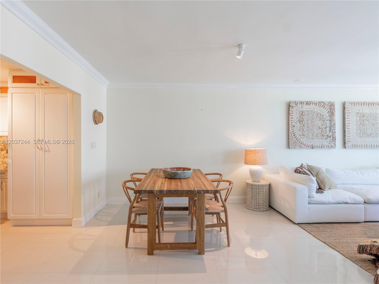 A dining area with a wooden table and chairs sits next to a white sofa — 5401 Collins Ave # 1013, Miami Beach FL 33140, MIAMI BEACH, FL