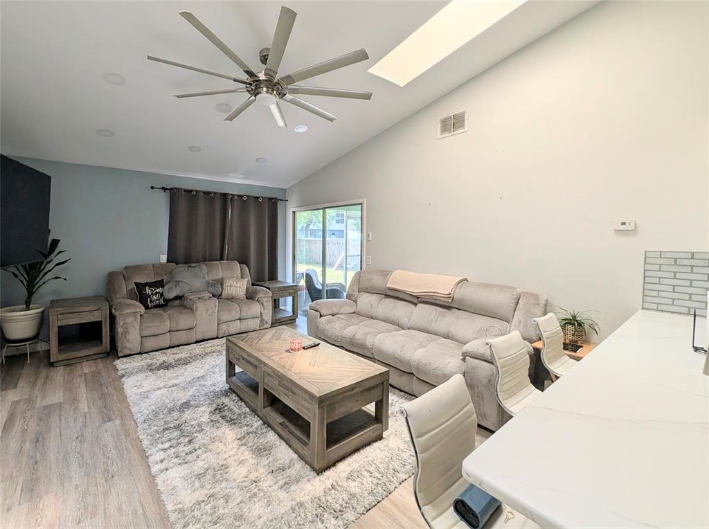 A living room features a vaulted ceiling, a ceiling fan, and a large area rug — 3140 WAINWRIGHT STREET, DELTONA, FL