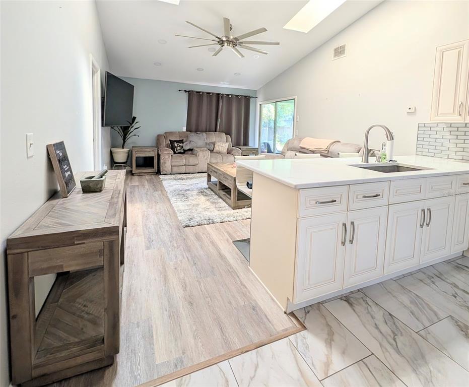 An open-concept living room and kitchen featuring light wood flooring, white cabinetry, and a ceiling fan — 3140 WAINWRIGHT STREET, DELTONA, FL