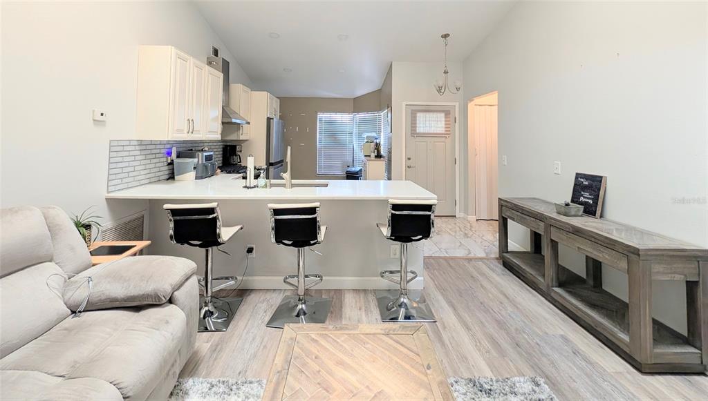 A kitchen with white cabinets and a breakfast bar overlooks a living area with wood-look flooring — 3140 WAINWRIGHT STREET, DELTONA, FL