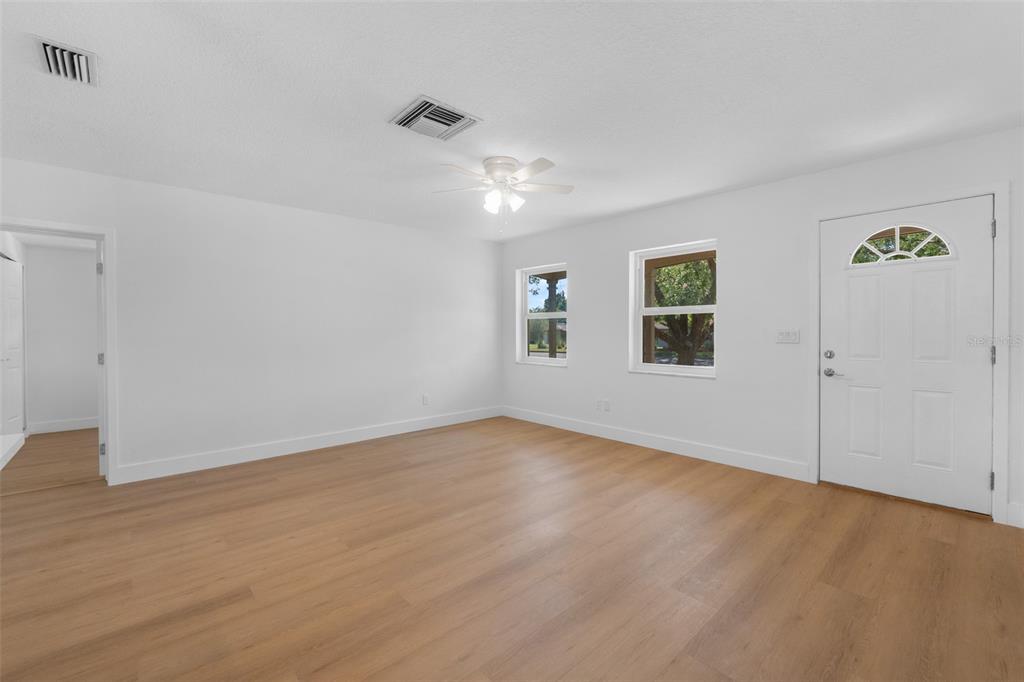 A bright, empty living room features white walls, light wood-look flooring, and a ceiling fan — 1524 PROVIDENCE BOULEVARD, DELTONA, FL