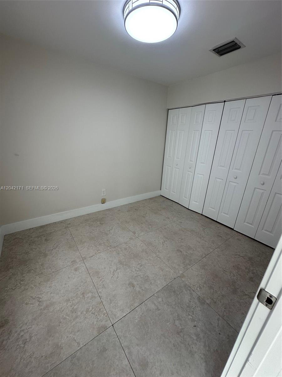 An empty room features light-colored walls, large square floor tiles, and a white closet — MIAMI, FL