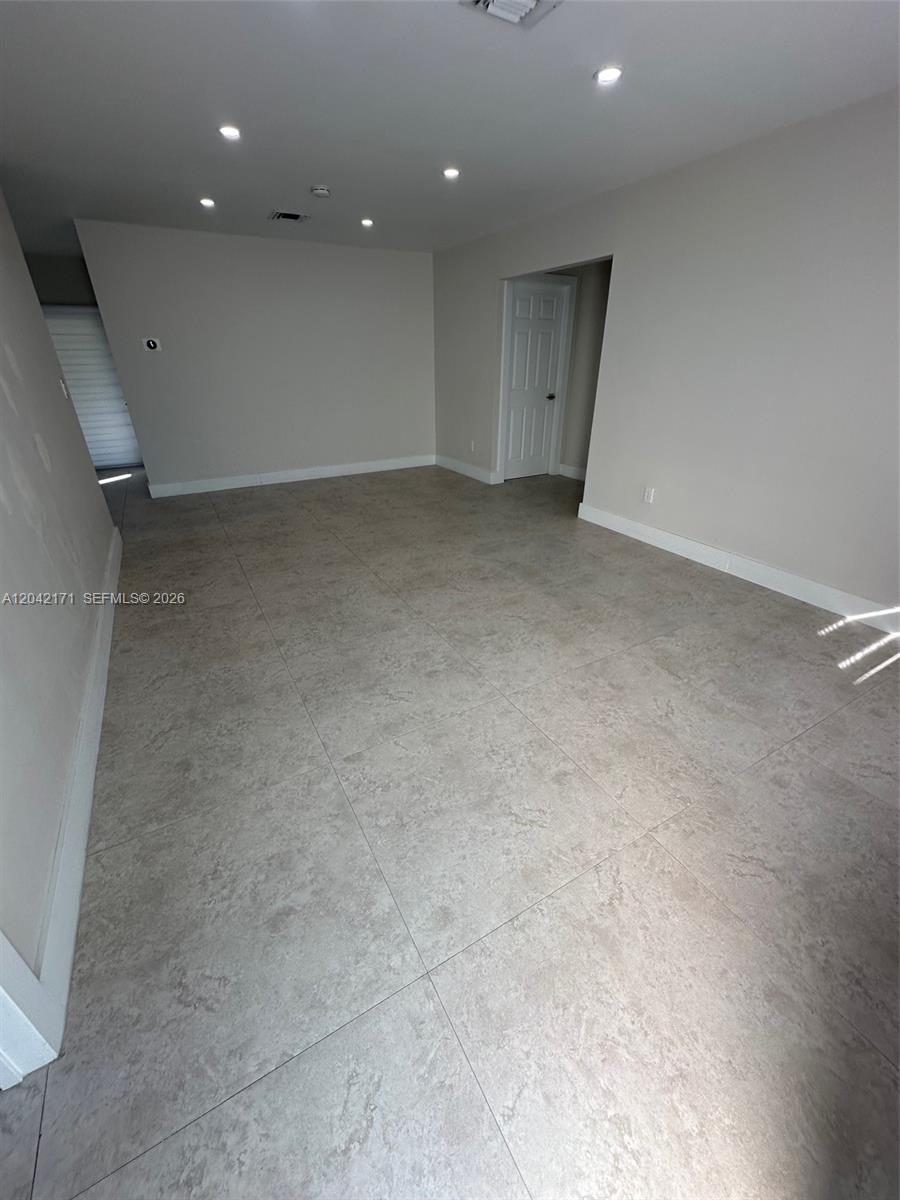 An empty room features light gray walls, recessed ceiling lights, and large beige floor tiles — MIAMI, FL