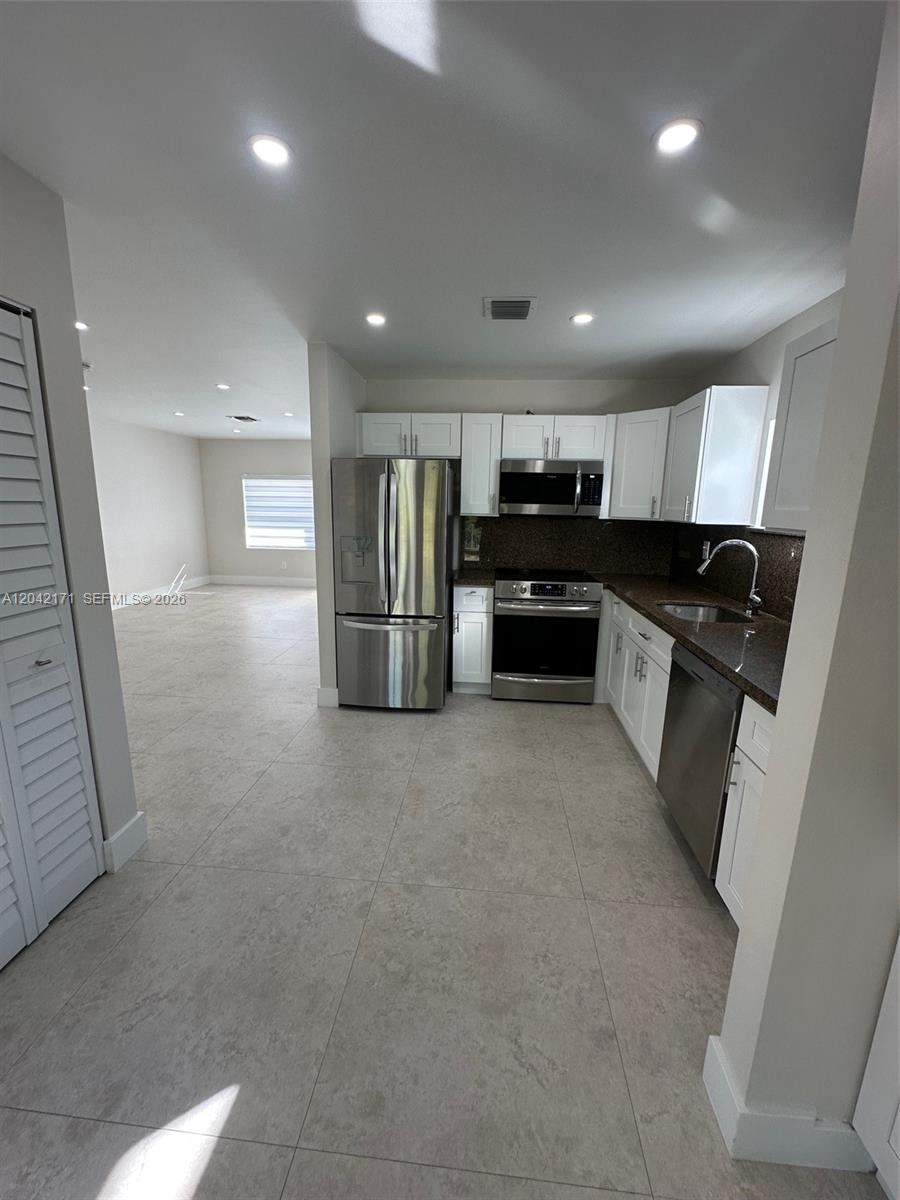 A kitchen with white cabinets, stainless steel appliances, and dark countertops opens to a living area — MIAMI, FL