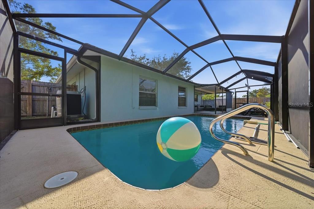 A swimming pool with a beach ball sits inside a screened-in lanai area — 5883 WHISTLEWOOD CIRCLE, SARASOTA, FL
